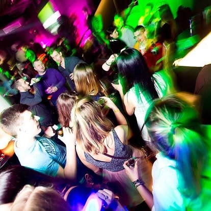A crowded dancefloor under vivid green and magenta club lights